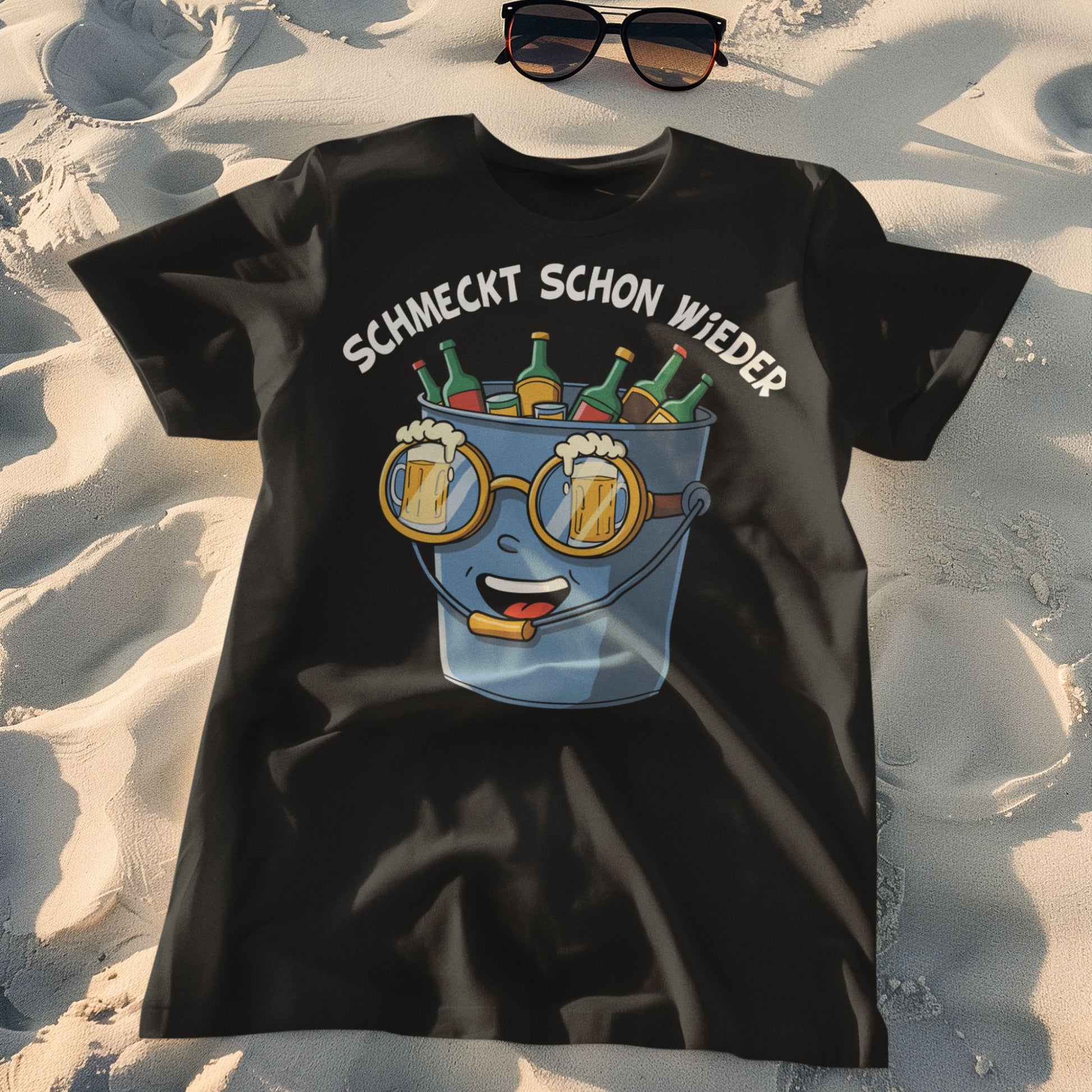 Schwarzes T-Shirt mit Saufeimer-Comic und Spruch „Schmeckt schon wieder“ – lustiges Unisex Partyshirt für Ballermann & Festival liegt auf dem Sand