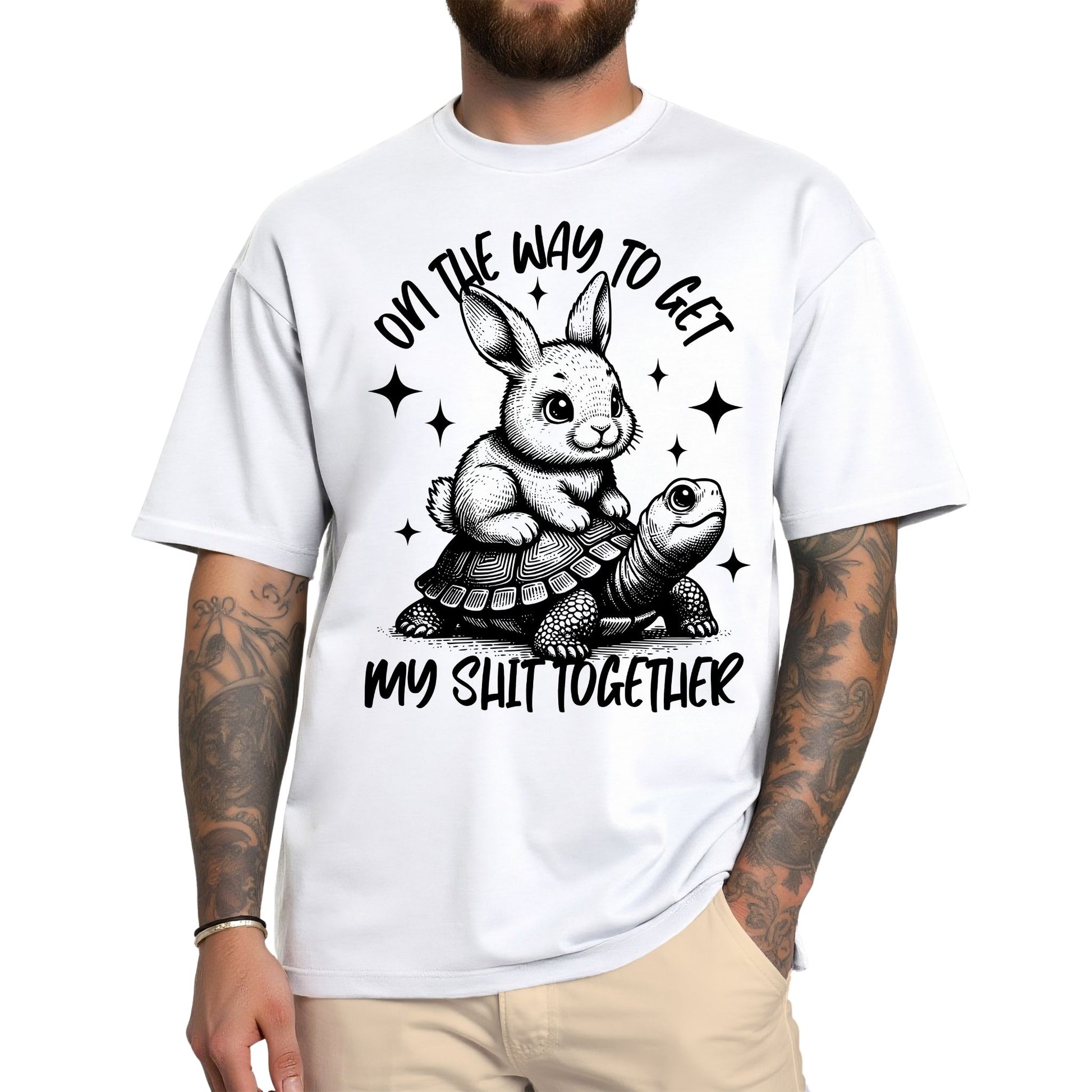 Weißes T-Shirt mit schwarzem Aufdruck: Ein Hase reitet auf einer Schildkröte mit dem Spruch „On the way to get my shit together“.