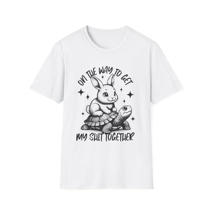 Weißes T-Shirt mit schwarzem Aufdruck: Ein Hase reitet auf einer Schildkröte mit dem Spruch „On the way to get my shit together“.
