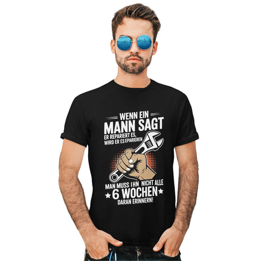 Mann trägt Schwarzes Reparatur Humor T-Shirt mit Spruch „Wenn ein Mann sagt, er repariert es…“ und Illustration einer Hand mit Schraubenschlüssel – erhältlich in Schwarz, Military Green und Grau
