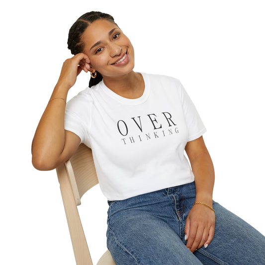 Frau trägt weißes T-Shirt mit schwarzem minimalistischen Schriftzug „OVERTHINKING“, sitzt entspannt auf einem Stuhl und lächelt
