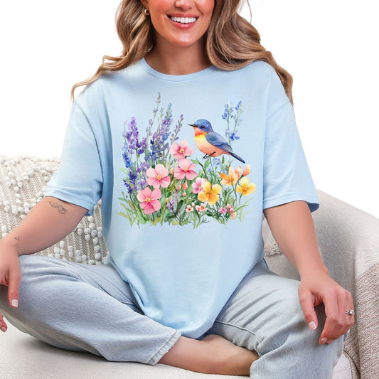 Frau trägt hellblaues  T-Shirt mit buntem Vogel und Blumenmotiv – Natur & Frühling Design Unisex