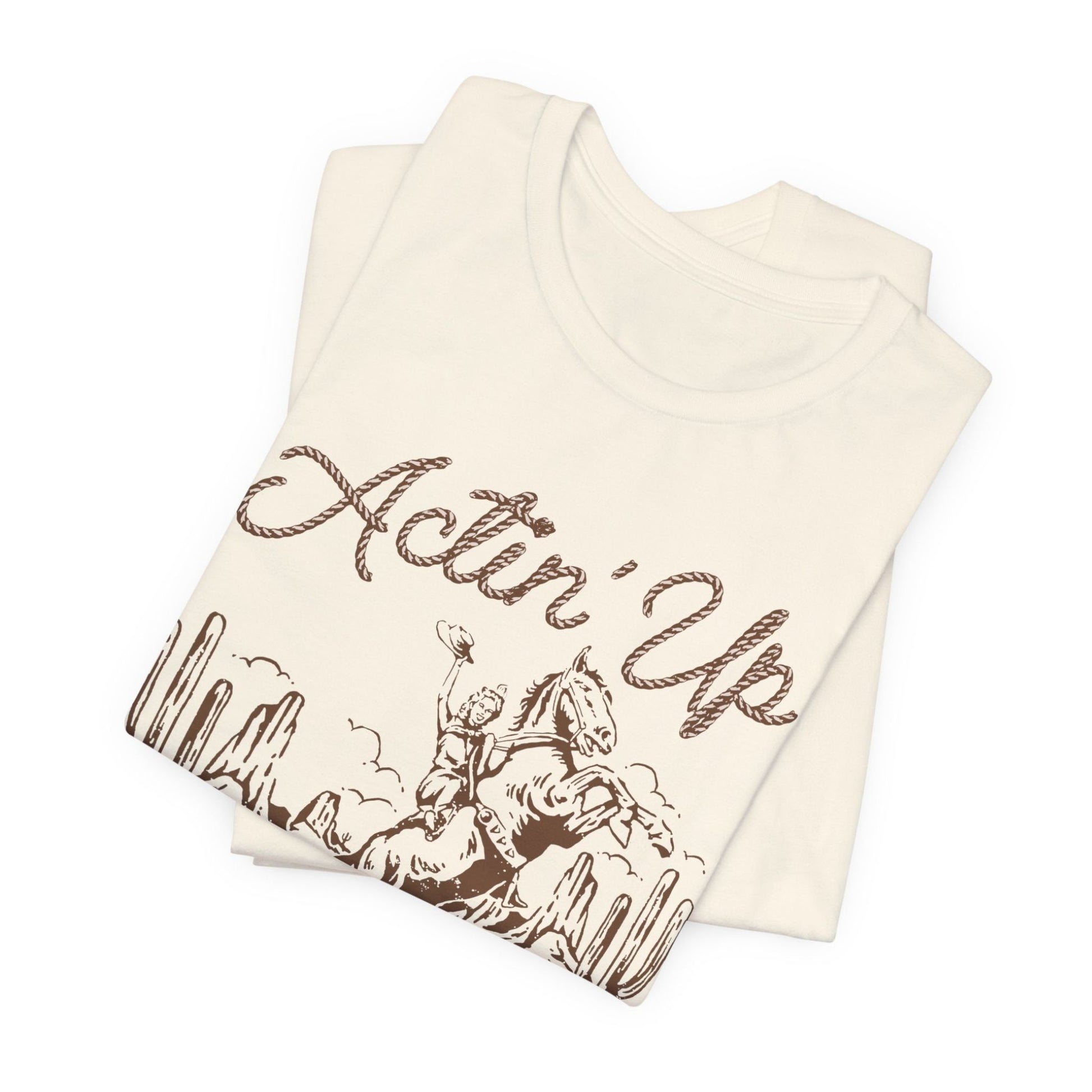 T-Shirt mit 'Actin Up' in Lasso-Schrift und Illustration einer reitenden Frau auf Pferd in der Wüste – Western-Style Design