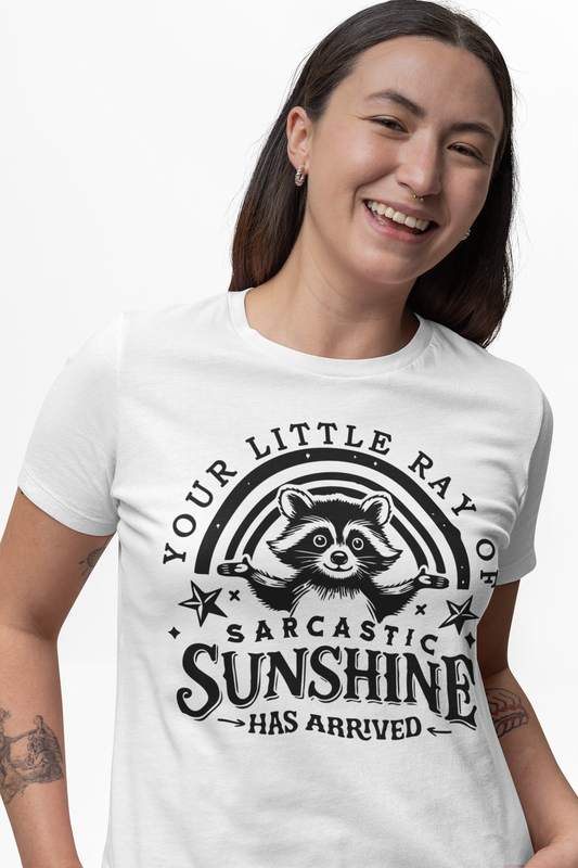 Weißes T-Shirt mit Waschbär und dem englischen Spruch „Your little ray of sarcastic sunshine has arrived“ in verspielter Schrift